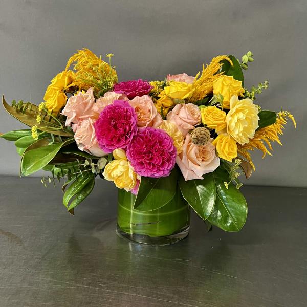 Mixed bouquet of pink, yellow, and peach flowers in a glass vase