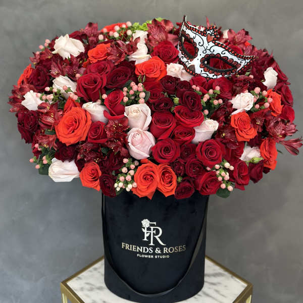 Large red and white rose arrangement in a black hatbox with a decorative mask