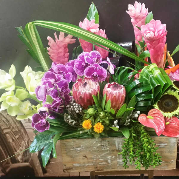 Tropical floral arrangement with orchids, protea, and bird of paradise in a wooden box