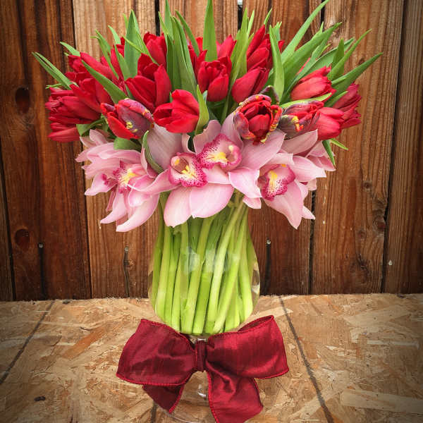 Bouquet of red tulips and pink orchids in a glass vase with a red bow