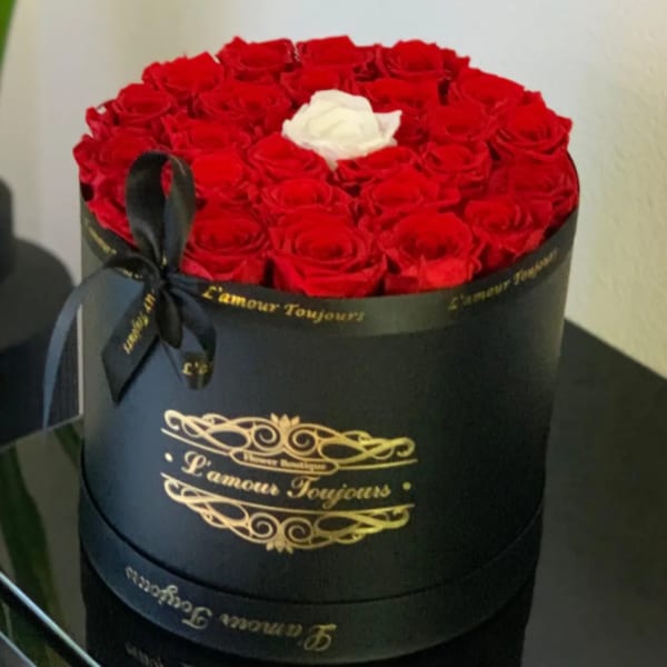Round box of red roses with one white rose on top and a black ribbon