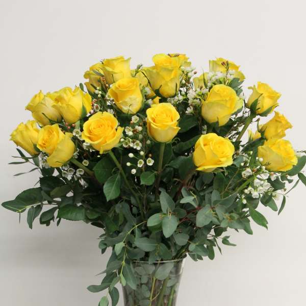 Yellow roses arranged in a clear glass vase with greenery