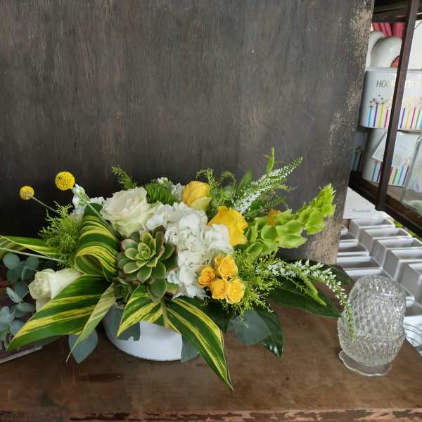 Low floral arrangement with white and yellow blooms in a white container