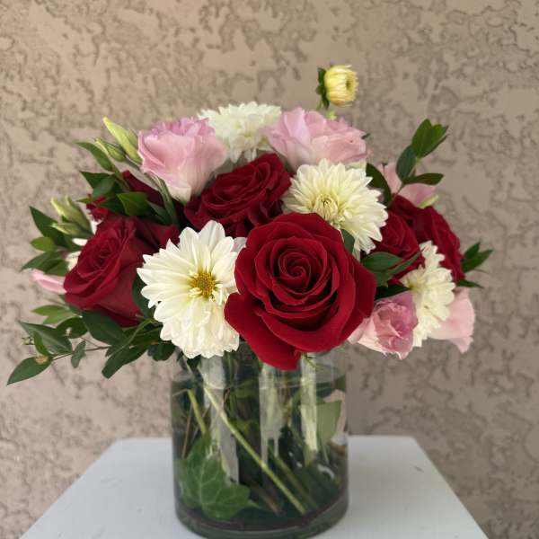 Bouquet of red roses, pink blooms, and white daisies in a glass vase