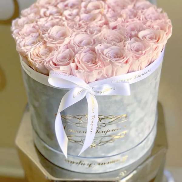 Round gray hatbox filled with tightly packed pale pink roses and tied with a white ribbon