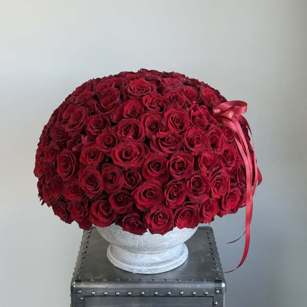 Large dome arrangement of red roses in a white pedestal vase with a red ribbon