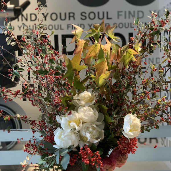 Tall arrangement of white flowers and red berry branches in a dark vase