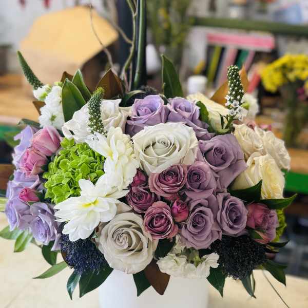 Lavender and white roses arranged in a white vase with white daisies
