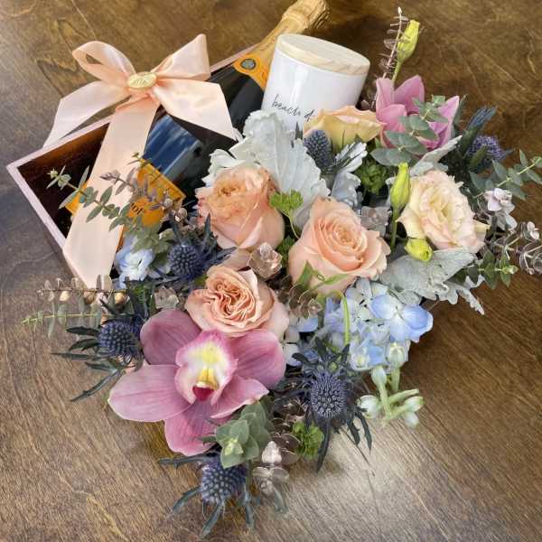 Bouquet with peach roses, pink orchid, and blue flowers beside a champagne bottle and candle