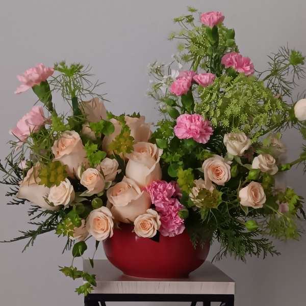 Pink and peach roses with carnations in a red vase