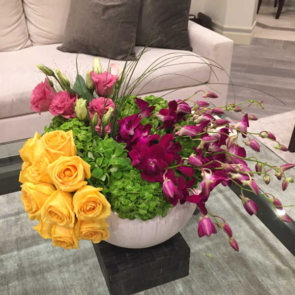 Mixed bouquet with yellow roses, pink lisianthus, and purple orchids in a white vase