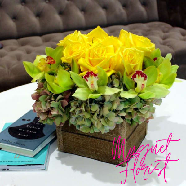 Yellow roses and green orchids in a square burlap box