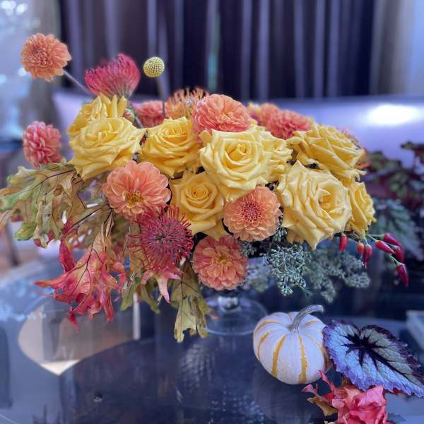 Yellow roses and peach dahlias in a low arrangement with autumn leaves