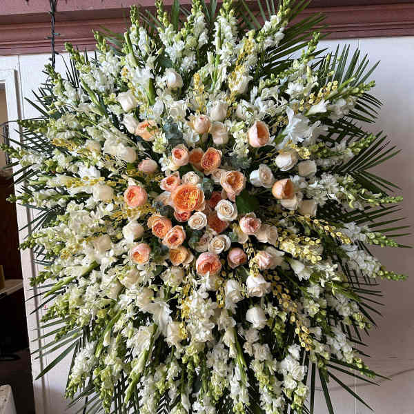 Large standing spray of white and peach roses with white blooms and palm fronds