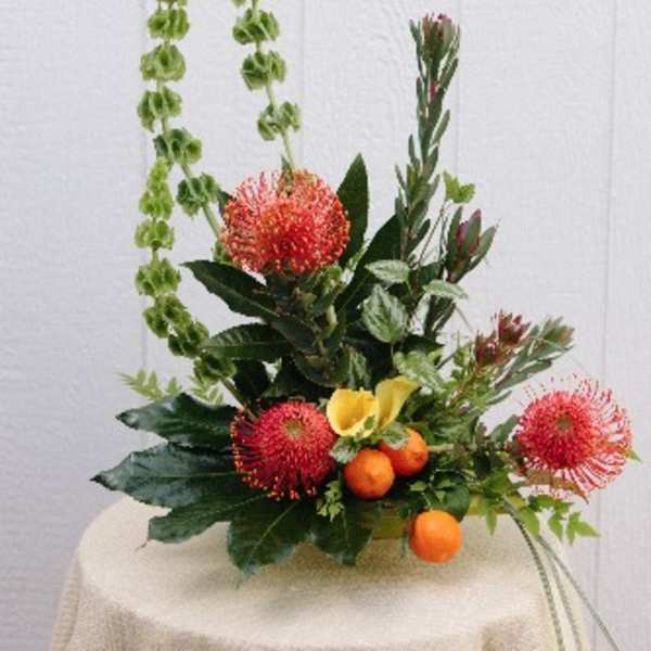 Tropical floral arrangement with red pincushion blooms and yellow calla lilies