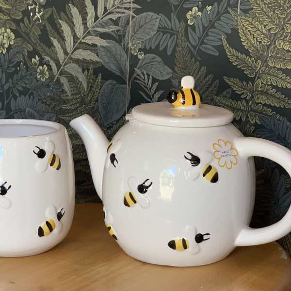 Bee-patterned ceramic mug and teapot on a wooden surface