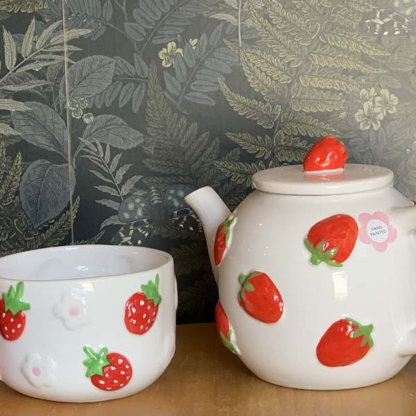 Strawberry-patterned ceramic teapot and matching cup on a table