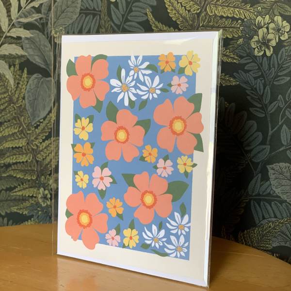 Floral greeting card with coral, yellow, white, and pink flowers on a blue background