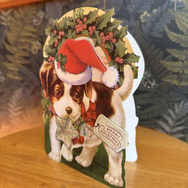 Christmas card with a puppy wearing a Santa hat and holly wreath
