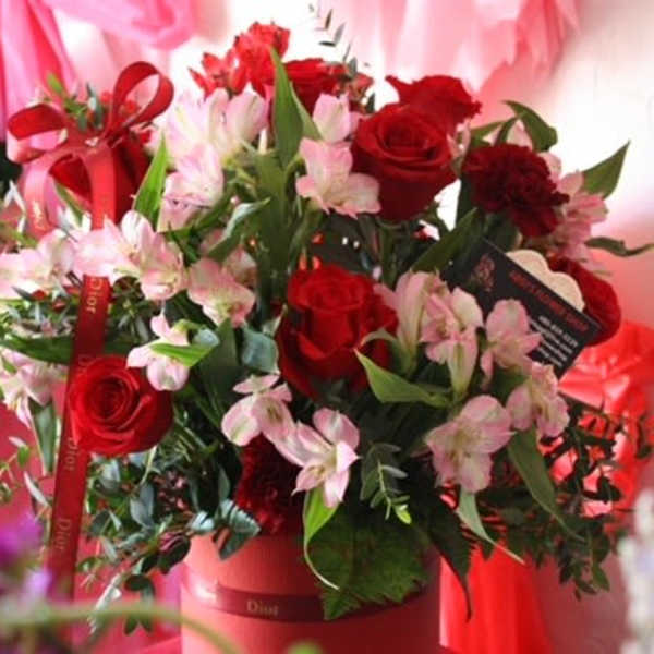 Red roses and pink lilies arranged in a red box with ribbon