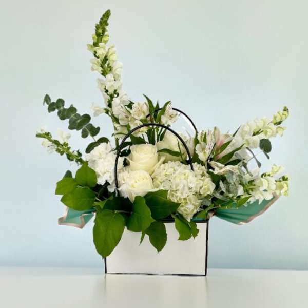 White floral arrangement in a white box with black handles