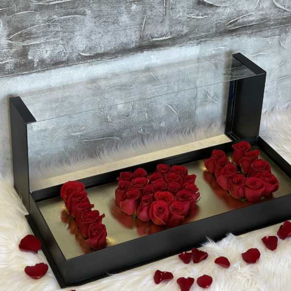 Red roses arranged in a black display box with scattered petals