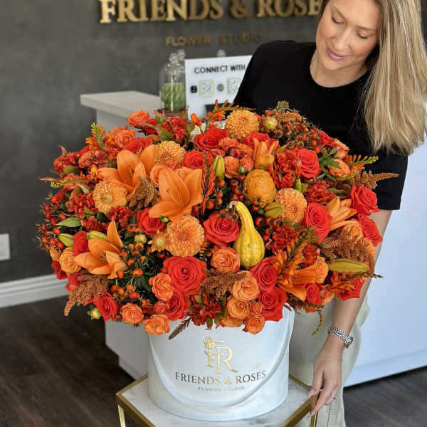 Large orange and red floral arrangement in a white hat box