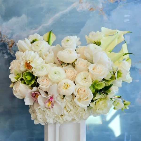 White floral arrangement in a tall white vase with calla lilies and roses