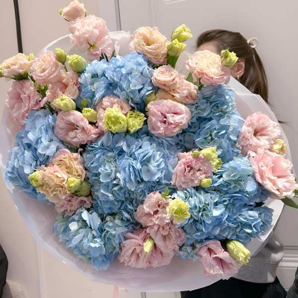 Large bouquet of blue hydrangeas and pink carnations wrapped in white paper