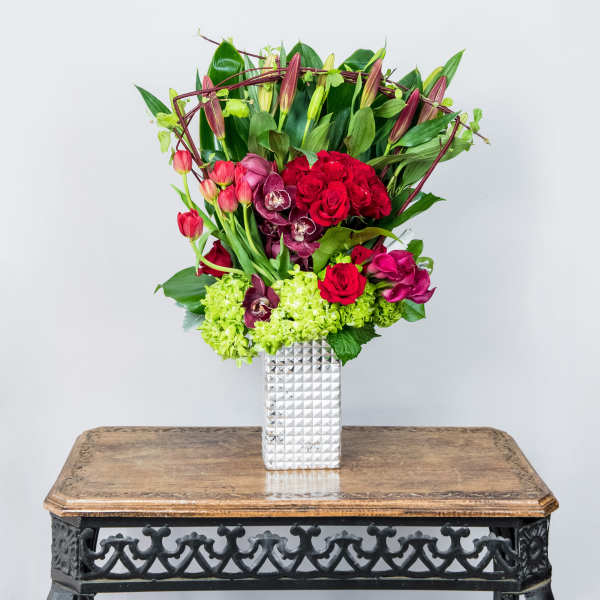 Bouquet of red roses, orchids, and tulips in a silver vase
