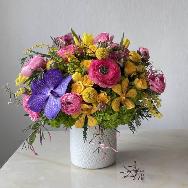 Bright mixed bouquet in a white textured vase with pink, yellow, and purple blooms