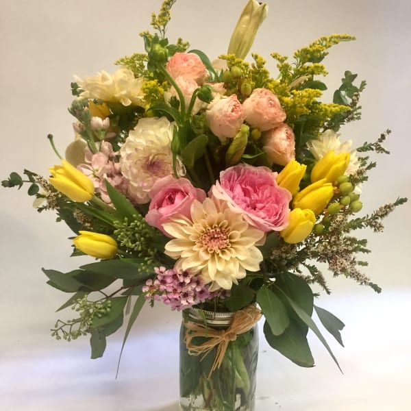 Mixed bouquet of pink roses, cream dahlias, and yellow tulips arranged in a glass mason jar vase.