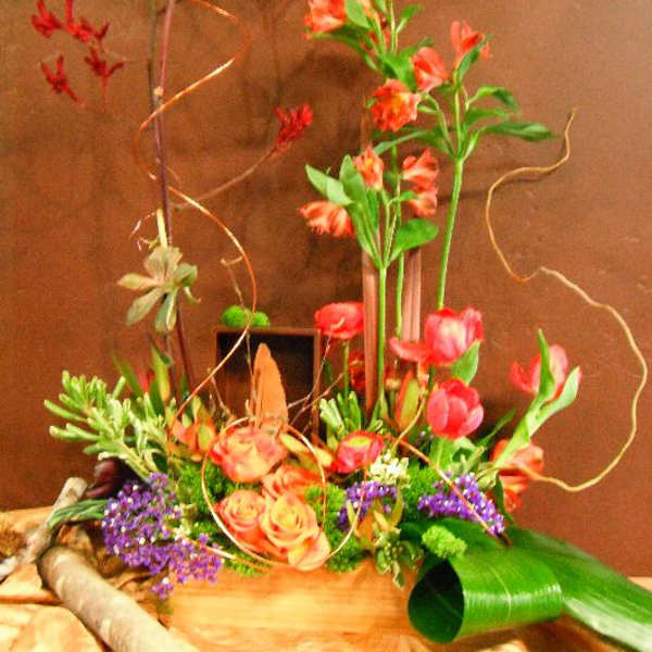 Tall floral arrangement with pink tulips, orange roses, and red tropical blooms