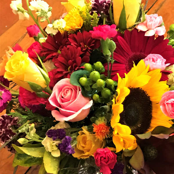 Mixed bouquet with sunflowers, roses, and gerbera daisies in a glass vase