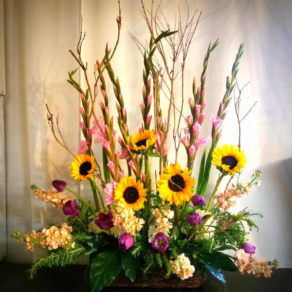 Tall floral arrangement with sunflowers, pink blooms, and purple tulips in a basket