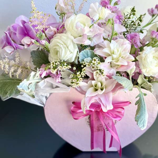 Pink and white floral arrangement in a heart-shaped box with a ribbon bow