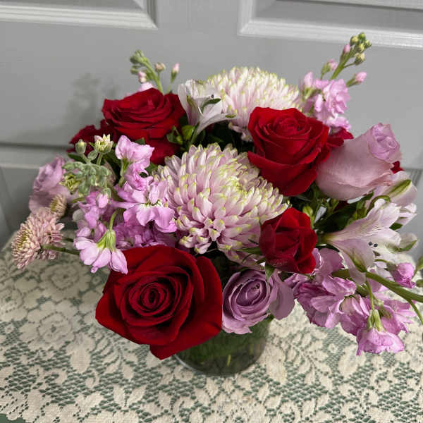 Bouquet of red and lavender roses with pink and white blooms in a glass vase