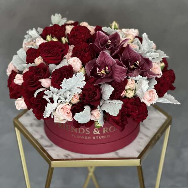 Round box arrangement of red roses, pink spray roses, and purple orchids