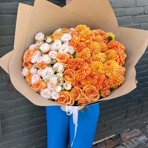 Large bouquet of orange and pale pink roses with dahlias wrapped in kraft paper
