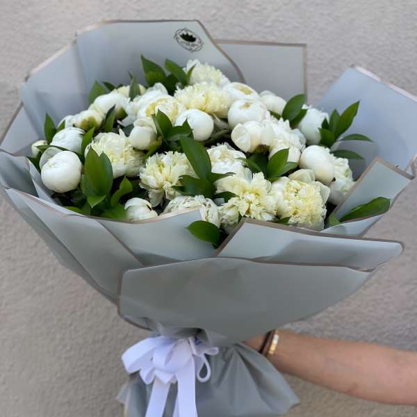 Handheld bouquet of white flowers wrapped in pale gray paper with a white ribbon