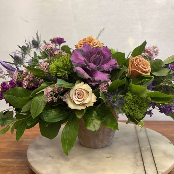 Mixed bouquet with roses, purple cabbage, and green thistle in a low vase