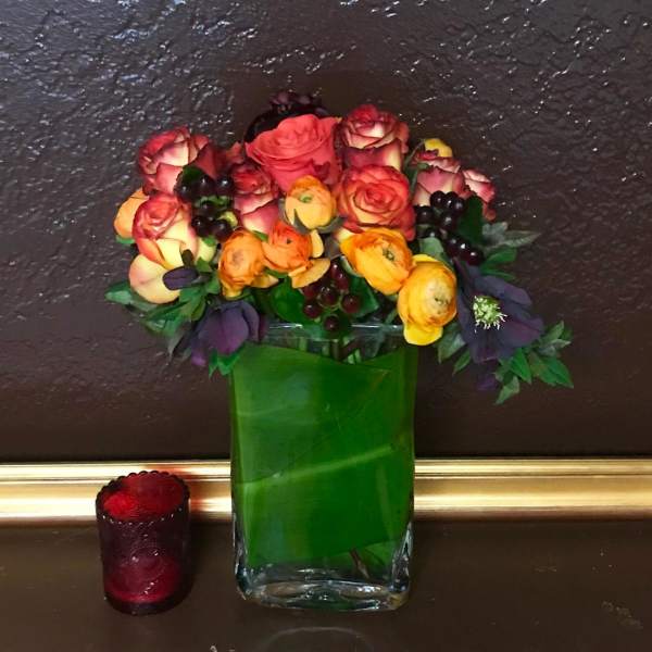 Mixed bouquet of roses and ranunculus in a green glass vase with a red candle nearby