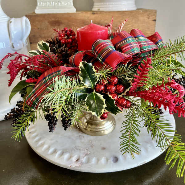 Holiday centerpiece with red candle, plaid ribbon, and evergreen sprigs