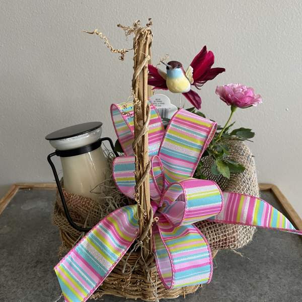 Basket arrangement with a pink flower, bird ornament, and striped ribbon