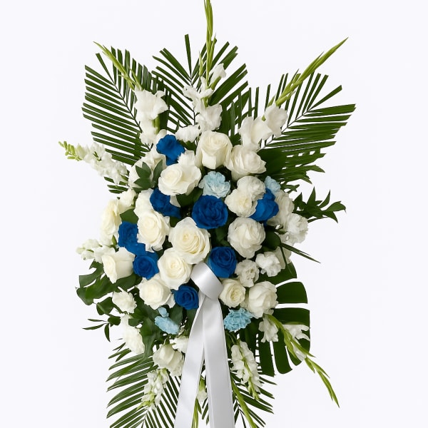 Standing floral spray of white and blue roses with palm fronds and a white ribbon