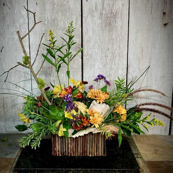 Mixed floral arrangement with yellow, purple, and orange blooms in a rustic container