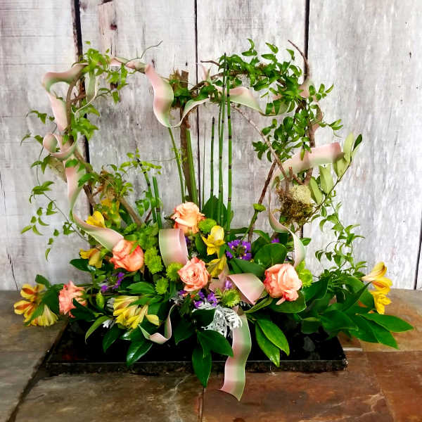 Floral arrangement with peach roses and yellow blooms on a decorative branch frame