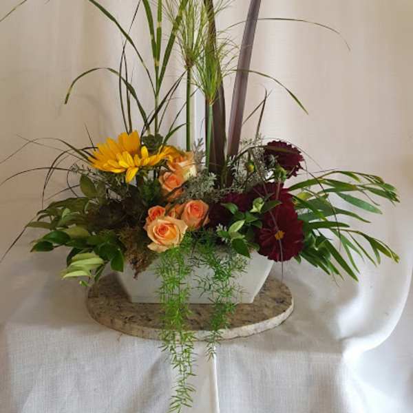 Mixed floral arrangement in a white rectangular vase with tall grass-like accents