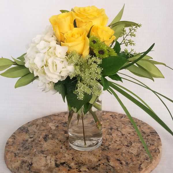 Yellow roses and white hydrangea in a clear glass vase