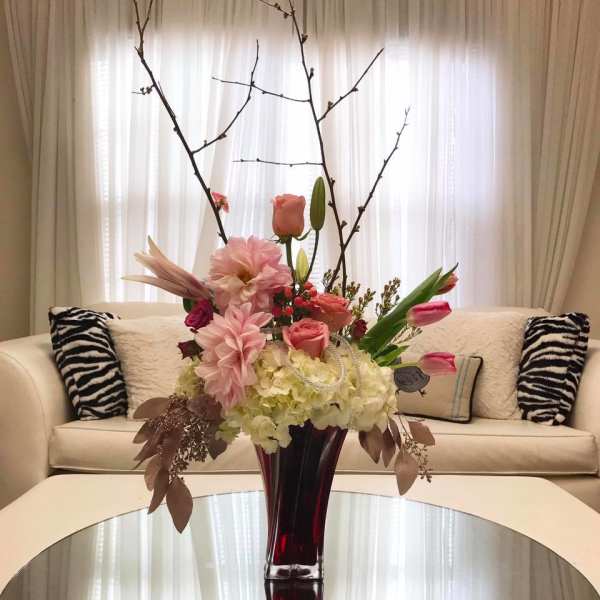 Tall floral arrangement with pink blooms in a red glass vase